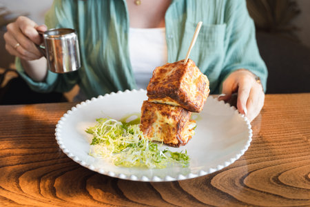 Trendy breakfast in hipster restaurant, cafe. Creative square-shaped croissant in the form of cube on skewer. Served with hot cheese in small gravy boat, sauceboat. Citylife meal, meating with friend.の写真素材
