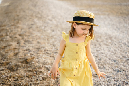 Little girl walking on beach, sea ocean shore in romantic yellow dress, straw hat. Playing in sand, blue waves. Family vacation travel leisure in hot summer coast. Sunny day relax in hotel resort.の写真素材