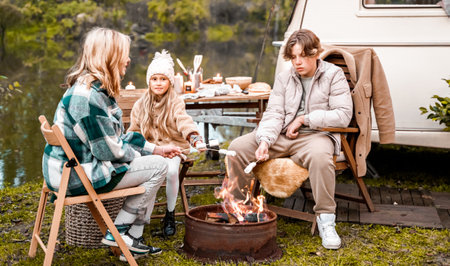 Children,family,brother sister fry marshmallows on fire. Picnic in nature. Wooden chair,table.Barbecue BBQ food. Holiday travel,vacation weekend dinner.Road lunch snack.Camper,house on wheels,trailer.の写真素材