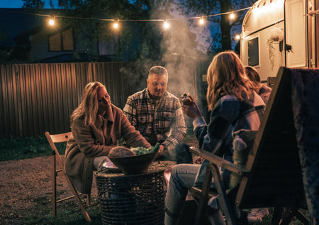 Family trailer travel. Children, brother sister, mom dad fry sausages on fire, eat hot dogs. Evening picnic in nature.Holiday barbecue BBQ food.Vacation weekend dinner.Road lunch.Camper,house on wheels.の写真素材