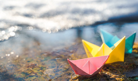 Multicolored paper boats. Colorful pink yellow blue orange ships in big spring snow puddle on winter street. Warm wet rainy weather, old grass. hello spring autumn. Children play, have fun outdoors.の写真素材