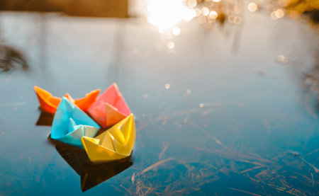 Multicolored paper boats. Colorful pink yellow blue orange ships in big spring snow puddle on winter street. Warm wet rainy weather, old grass. hello spring autumn. Children play, have fun outdoors.の写真素材