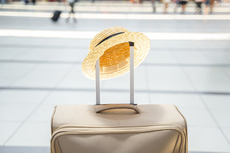 Straw hat on big suitcase, bag in airport terminal. Waiting for boarding to flight. Family vacation travel. Luggage baggage check in departure hall. Summer sea tour. Arrival for holiday trip.の写真素材
