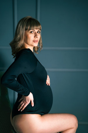 Pregnant woman with big belly in black bodysuit, lingerie. Sexy attractive girl photoshoot in studio. Happy pregnancy, maternity, preparation. baby expectation. Beautiful tender young mother.の写真素材