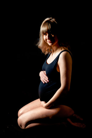 Pregnant woman with big belly in bodysuit, lingerie on black background. Sexy attractive girl photo shoot in studio. Happy pregnancy,maternity,preparation.Baby expectation.Beautiful tender young mother.の写真素材