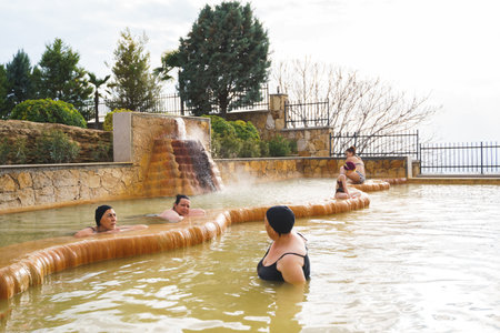 Family, dad and children bathe, swim in outdoor dirty hot springs. Thermal water bath pool and healthy natural, clay and yellow green mud. Spa wellness relax family winter vacation in mountain hotel.のeditorial素材
