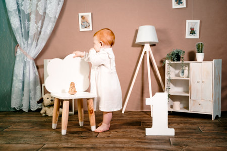 Little redhead baby girl celebrate first birthday anniversary. 1 year family party Professional photoshoot in photo studio. Cute adorable red hair kid in white vintage dress. Children's room at home.の写真素材