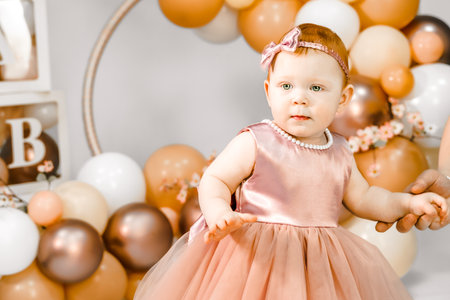 Little redhead baby girl celebrate first birthday anniversary. 1 year family baloons party. professional photography. photo studio. Cute adorable red hair kid. Red holiday dress. Children's home room.の写真素材