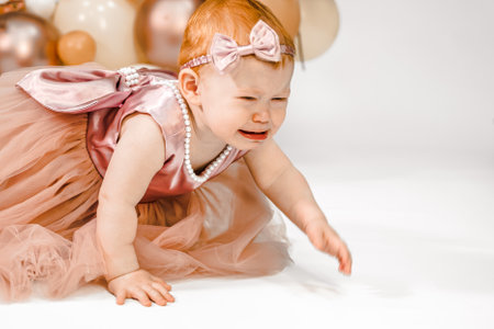 Little crying unhappy redhead baby girl celebrates first birthday anniversary. 1 year family party Professional photoshoot in photo studio. Cute adorable red hair kid in pink dress.Home children room.の写真素材