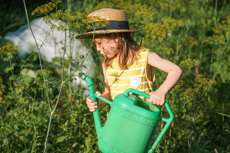 Farmer girl in yellow dress. Little vegetables gardener farming in garden. Big green watering can water fresh cucumbers seedlings. Harvest help work. Cultivation healthy organic food, countryside.の写真素材
