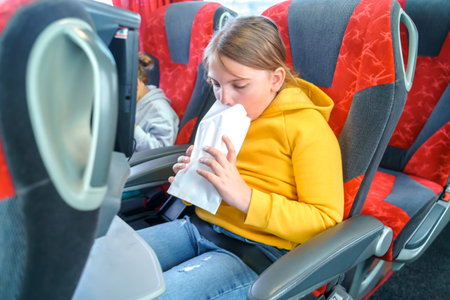 Girl is sick, vomits in bag. Bus road traveling. Girl kid feels bad, rides on large comfortable sightseeing excursion bus. Sitting watching movie cartoon on chair screen. entertainment media system.の写真素材
