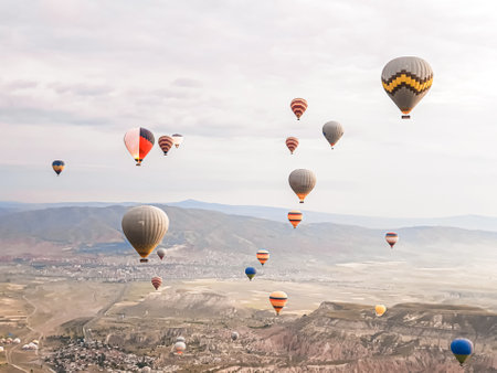 Flying in the sky many bright colored beautiful balloons into the air in Cappadocia in the mountains early at sunrise, dawn. Filling balloon with hot air from burner, big basket. Tourists excursion, cloud flight.の写真素材