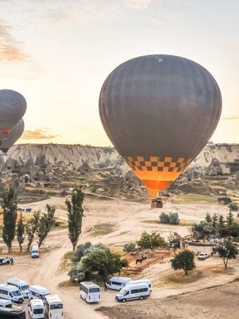 Flying in the sky many bright colored beautiful balloons into the air in Cappadocia in the mountains early at sunrise, dawn. Filling balloon with hot air from burner, big basket. Tourists excursion, cloud flight.の写真素材
