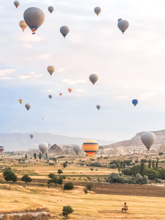 Flying in the sky many bright colored beautiful balloons into the air in Cappadocia in the mountains early at sunrise, dawn. Filling balloon with hot air from burner, big basket. Tourists excursion, cloud flight.の写真素材