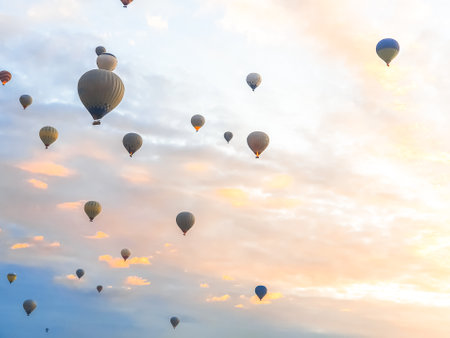 Flying in the sky many bright colored beautiful balloons into the air in Cappadocia in the mountains early at sunrise, dawn. Filling balloon with hot air from burner, big basket. Tourists excursion, cloud flight.の写真素材