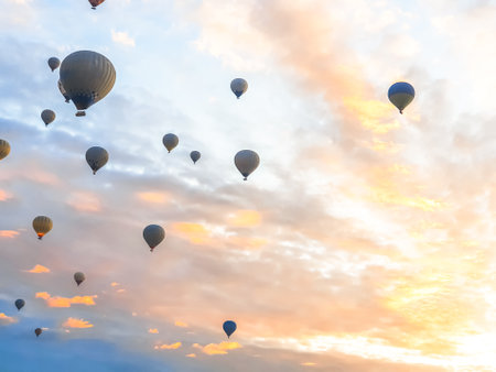 Flying in the sky many bright colored beautiful balloons into the air in Cappadocia in the mountains early at sunrise, dawn. Filling balloon with hot air from burner, big basket. Tourists excursion, cloud flight.の写真素材