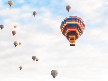 Flying in the sky many bright colored beautiful balloons into the air in Cappadocia in the mountains early at sunrise, dawn. Filling balloon with hot air from burner, big basket. Tourists excursion, cloud flight.の写真素材