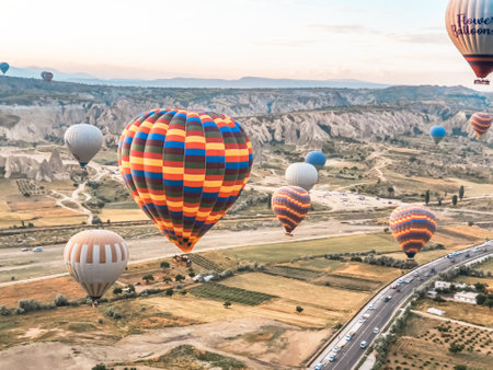 Flying in the sky many bright colored beautiful balloons into the air in Cappadocia in the mountains early at sunrise, dawn. Filling balloon with hot air from burner, big basket. Tourists excursion, cloud flight.の写真素材