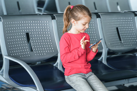 Kid, teen girl waiting for plane flight in departure hall. Sitting on chairs, playing computer games in gadgets, mobile phone, tablet. Chatting in social networks, what video. study online.の写真素材
