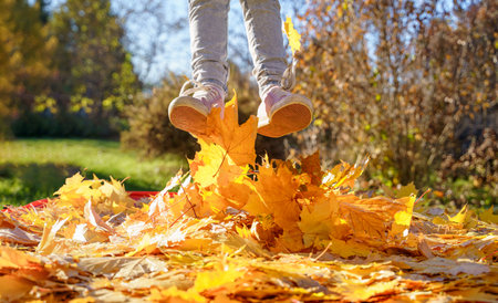 Girl kid jumping on trampoline with autumn leaves. Bright yellow orange maple foliage. Child walking, having fun, playing in fall backyard. Outdoor funny happy season family activity in autumn park.の写真素材