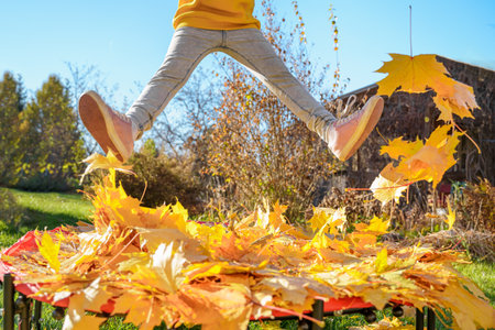 Girl kid jumping on trampoline with autumn leaves. Bright yellow orange maple foliage. Child walking, having fun, playing in fall backyard. Outdoor funny happy season family activity in autumn park.の写真素材