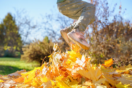 Girl kid jumping on trampoline with autumn leaves. Bright yellow orange maple foliage. Child walking, having fun, playing in fall backyard. Outdoor funny happy season family activity in autumn park.の写真素材