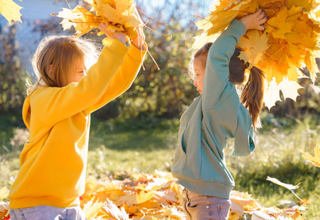 Girls kids playing jumping on trampoline with autumn leaves. Bright yellow orange maple foliage. Children walking, having fun in fall backyard. Outdoor funny happy season family activity, autumn park.の写真素材