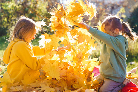 Girls kids playing jumping on trampoline with autumn leaves. Bright yellow orange maple foliage. Children walking, having fun in fall backyard. Outdoor funny happy season family activity, autumn park.の写真素材