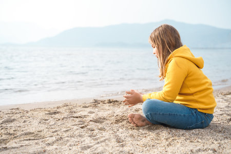 Lonely beautiful sad girl teenager sits thoughtfully on sand sea beach. Dreams, anxiety, worries about the future, school friends, parents. Teen bullying, psychological problems in adolescent puberty period.の写真素材