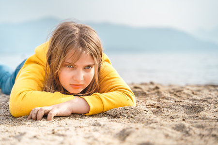 Lonely beautiful sad girl teenager lying thoughtfully on sand sea beach. Dreams, anxiety, worries about the future, school friends, parents. Teen bullying, psychological problems in adolescent puberty period.の写真素材