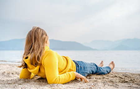 Lonely beautiful sad girl teenager lying thoughtfully on sand sea beach. Dreams, anxiety, worries about the future, school friends, parents. Teen bullying, psychological problems in adolescent puberty period.の写真素材