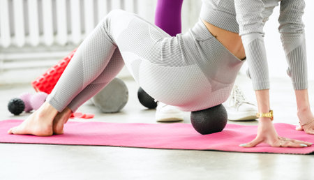 Slim woman training with yoga coach. Private lessons with personal trainer, fitness instructor. Workout, exercises at home on fitness mat. Sports equipment, resistance rubber, massage peanut ball.の写真素材