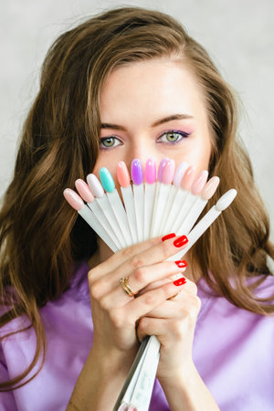 Professional master manicurist with multi-colorednail polish samples paletteat in beauty salon. Manicure service, hands treatments, procedures for nails, fingers. cuticle oil, gel uv lamp, gloves.の写真素材