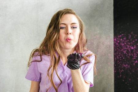 Professional master manicurist in black gloves, purple uniform with pink glitter for manicure at...