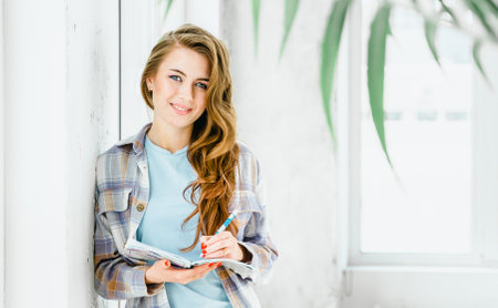 Young beautiful long haired college student girl in casual shirt with notebook, pen. Businesswoman making notes in organizer. Content portrait photo shoot for advertising in social networks, website.の写真素材