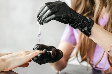 Professional master manicurist at beauty salon. Manicure cuticle oil service, hands treatments, procedures for nails, fingers massage. Multi-colored nail polish, samples palette, gel uv lamp, gloves.の写真素材
