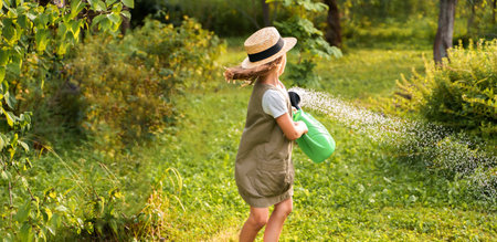 Farmer girl in summer straw hat. Little gardener farming spinning, having fun in garden with big green watering can water fresh grass. Harvest help work. Cultivation healthy organic food, countryside.の写真素材