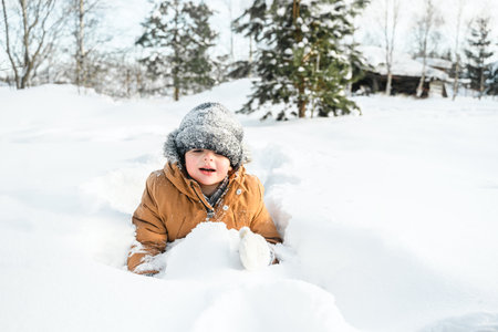 Little cute boy in black hat,orange jacket is lying,playing in snow. Kid walking in beautiful frozen...