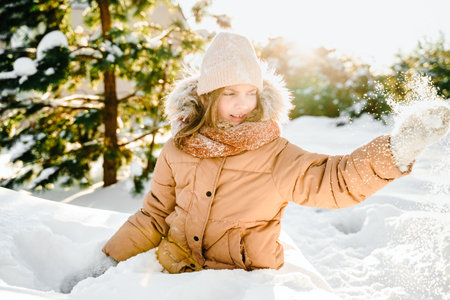 Little cute girl in beige hat,orange scarf snood is lying,playing in snow. Kid walking in beautiful...