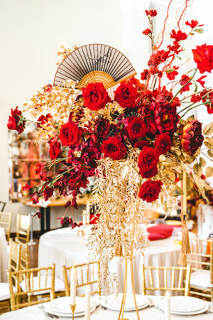 Floral arrangement, festive bouquet, table decoration for Chinese New Year party celebration in restaurant. Traditional red gold color decor. Roses,poppies,fans,candles,tassels. Chinese lunar calendar.の写真素材