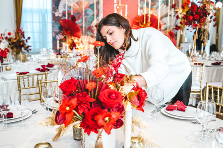 Red gold color flower decor for Chinese New Year celebration. Girl woman florist, decorator, organizer of events, parties, wedding planner making floral arrangement, festive bouquet, table decoration.の写真素材
