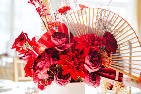 Floral arrangement, festive bouquet, table decoration for Chinese New Year party celebration in restaurant. Traditional red gold color decor. Roses,poppies,fans,candles,tassels. Chinese lunar calendar.の写真素材