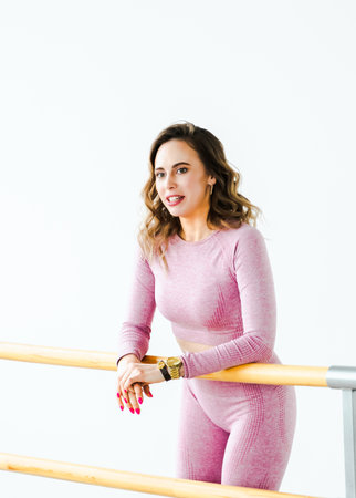 Slim ballerina woman girl in pink tracksuit. Stretching at ballet machine, showcasing dance athletic flexibility. Dancer trains in dance hall of fitness club. Sports training workout with instructor.の写真素材