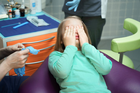 Little scared girl sitting in chair in dentist doctor office. Kid,child afraid of tooth extraction, teeth treatment, examine with open mouth. Dental clinic check-up. Reclined position. Dentist gloves.の写真素材