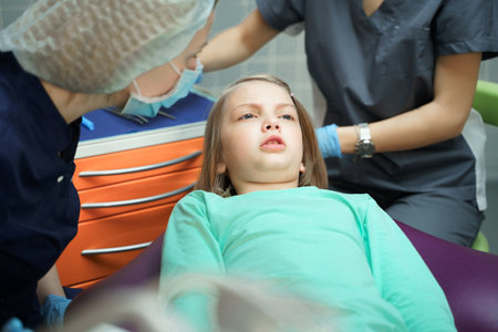 Little scared girl sitting in chair in dentist doctor office. Kid,child afraid of tooth extraction, teeth treatment, examine with open mouth. Dental clinic check-up. Reclined position. Dentist gloves.の写真素材