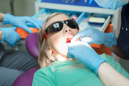 Little scared girl sitting in chair in dentist doctor office. Protective safety sunglasses. Kid,child afraid of tooth extraction, teeth treatment. Open mouth. Dental clinic check-up.Reclined position.の写真素材