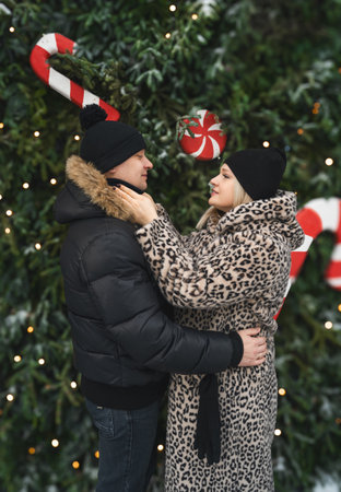 Love romantic couple love story. Man hugging woman, kissing girl in Christmas winter fur trees decoration. Romantic date. Walking, having fun. Stylish clothes, fur leopard print coat, black jacket, hat.の写真素材