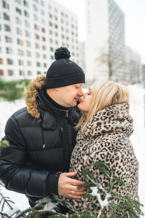 Love romantic couple love story. Man hugging woman, kissing girl in Christmas winter fur trees decoration. Romantic date. Walking, having fun. Stylish clothes, fur leopard print coat, black jacket, hat.の写真素材