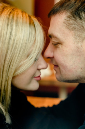 Love romantic couple love story. Man hugging woman, kissing blonde girl in cozy coffee shop cafe. Romantic family date. Sitting at window table in restaurant. Intimate romance atmosphere.の写真素材