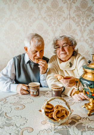Elderly senior romantic love couple drinking tea with cookies from samovar. Old retired man woman...